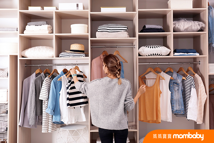 Woman choosing outfit from large wardrobe closet with stylish clothes and home stuff